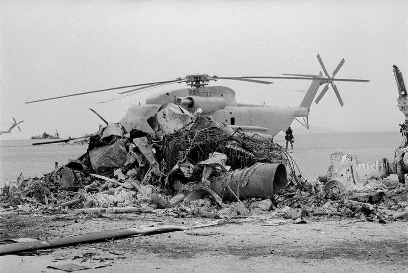 Неповреждённый вертолёт стоит на земле за обгоревшими остатками второго американского вертолёта в иранской пустыне Дешт-э-Кавир. 26 апреля 1980 года.