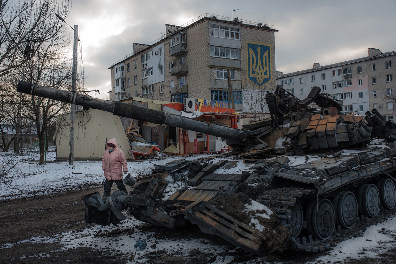 Сгоревший украинский танк, стоящий на фоне торца дома с нарисованным гигантским гербом Украины.