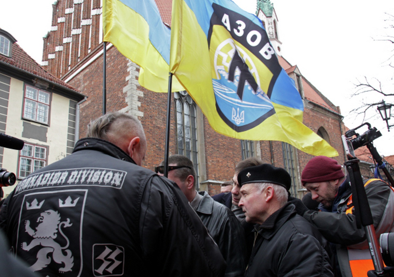 Люди с флагами украинского националистического добровольческого батальона «Азов»* участвуют в шествии латышского легиона «Ваффен-СС» в Риге.