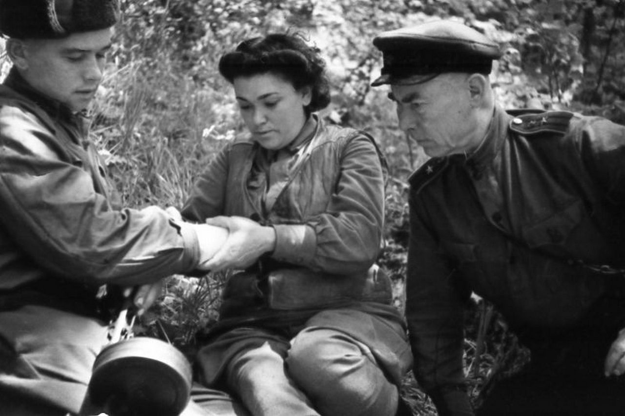 Медик специальной разведгруппы «Соколы» ОМСБОН НКВД СССР перевязывает раненого в руку партизана.