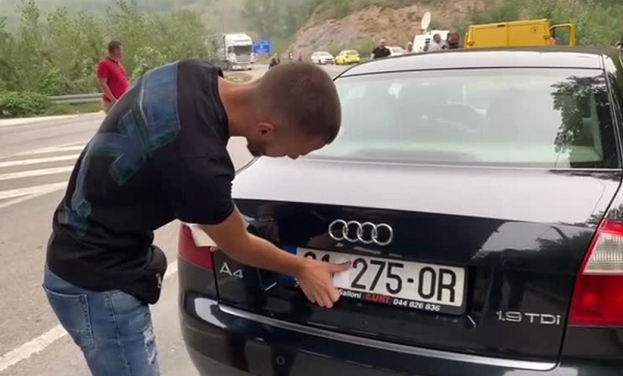 Водитель заклеивает на автомобильных номерах символы Сербии.