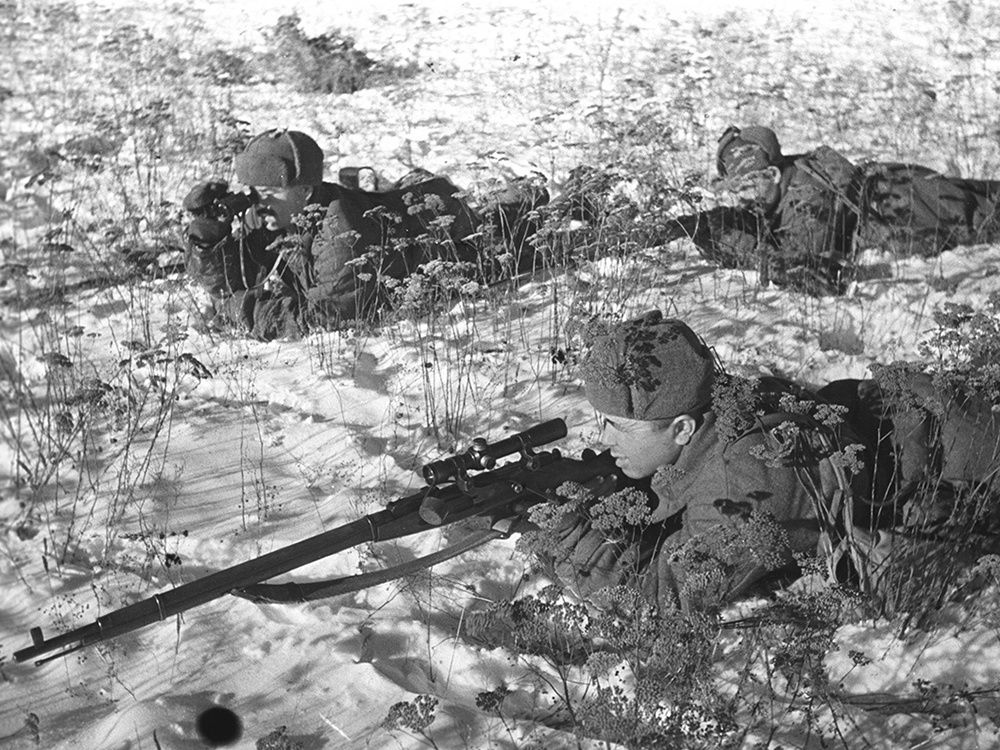 Советский снайпер в плащ-накидке со снайперской винтовкой Мосина, оснащенной оптическим прицелом ПЕ.